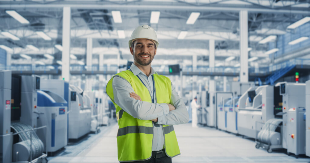 Mitarbeiter in Wanrweste und mit Helm in einer Produktionshalle